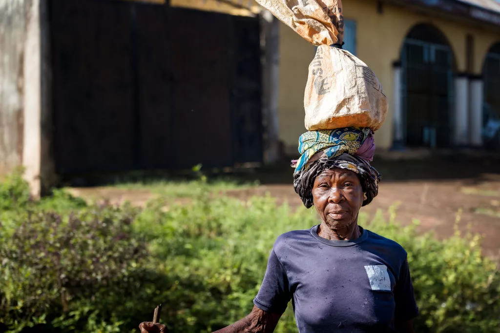 Nigerian woman looks at camera carrying bag of food on her head - Vision Africa.