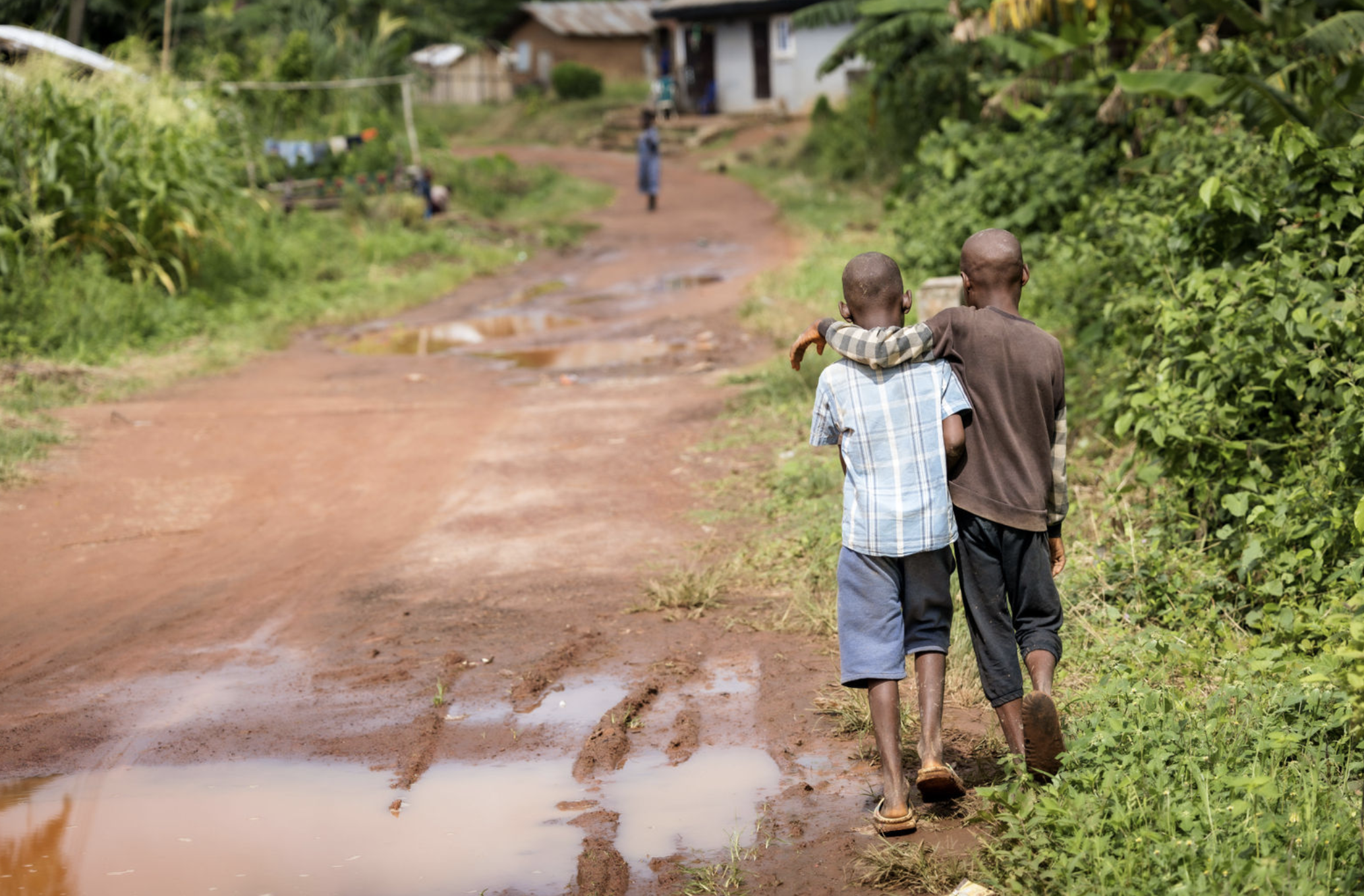 Two kids walking with arms around each other in an African village.